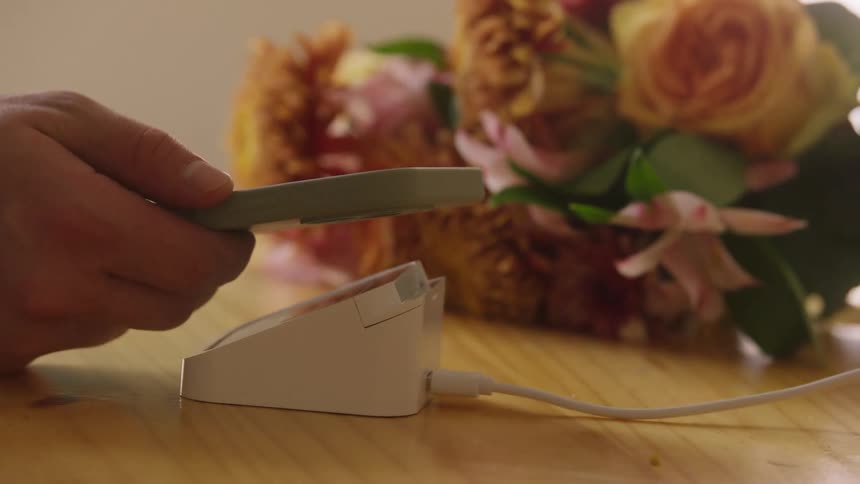 Hand holding smartphone makes contactless payment at pos terminal with flowers in the background