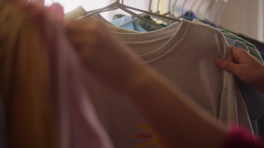 A woman sorts through numerous shirts hung from a rack on clothes hangers