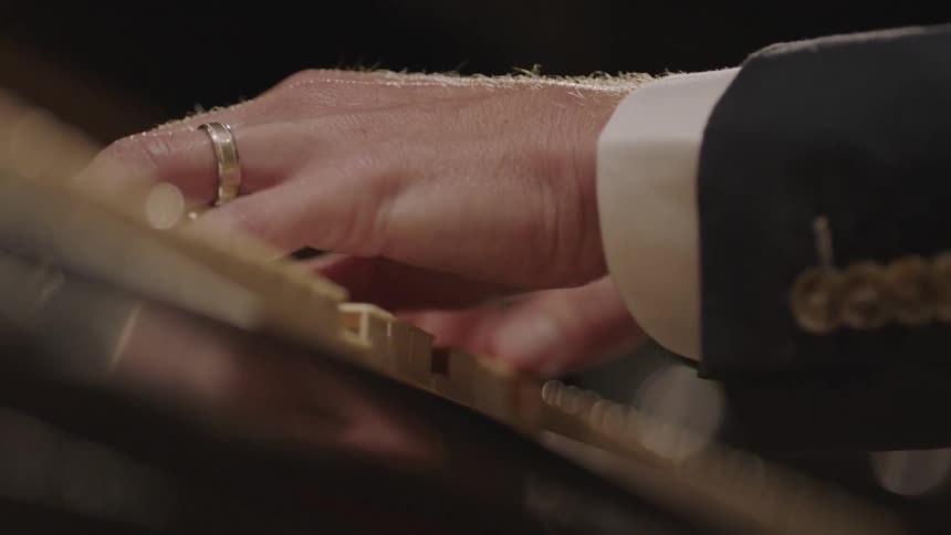 A man wearing a wedding ring plays piano