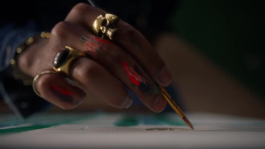 Hand holding a paintbrush stained with paint adds details to the canvas