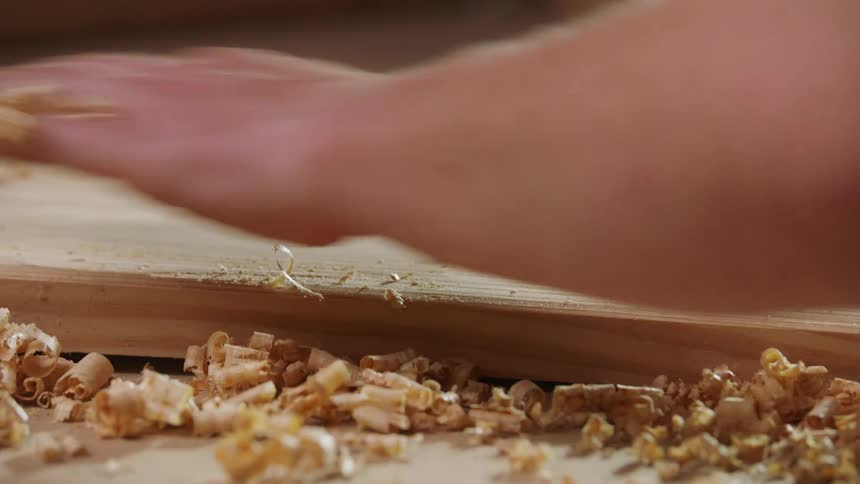 A hand sweeps wood shavings off a wooden board