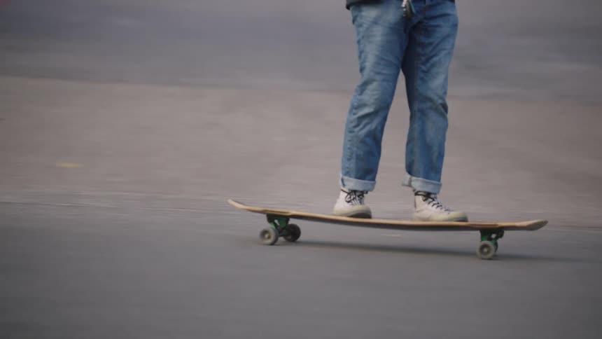 Person in white sneakers rides longboard on paved road with sidewalk and dry vegetation in background