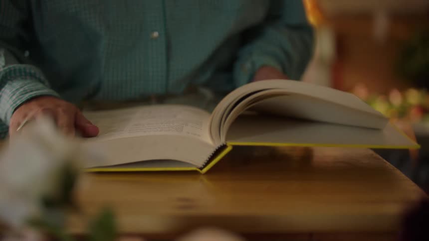 A person in a blue shirt opens a thick yellow book on a wooden table and flips through the pages
