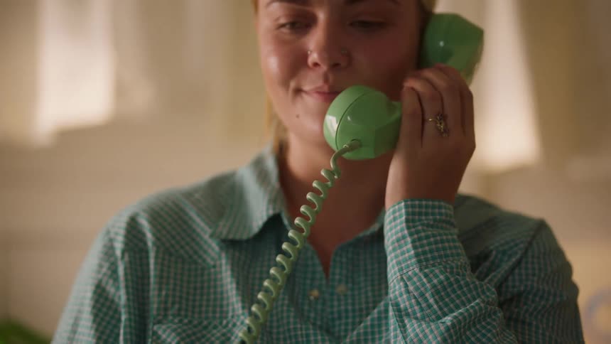 Woman answers the phone with a green handset while smiling during the call