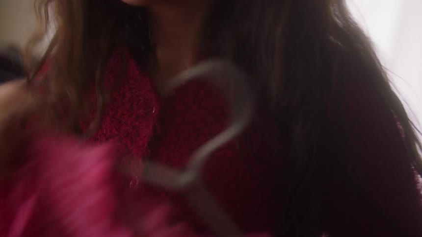 A woman browses through a rack of clothes and holds a pink patterned top against her chest