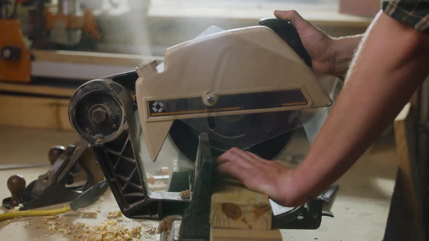 Person operating circular saw in woodworking shop cutting wood on workbench surrounded by tools