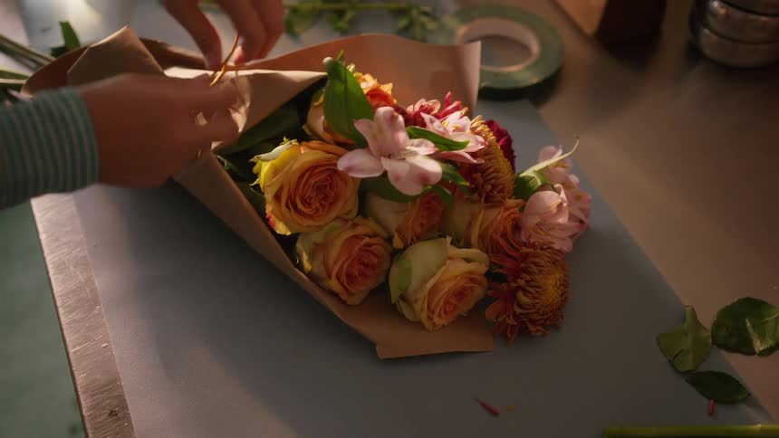 A person tying up a bouquet of flowers in a room