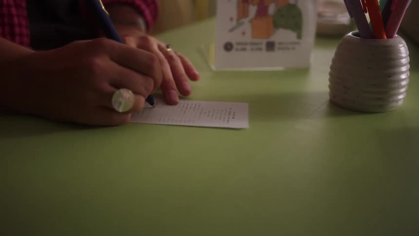 A person signs a receipt with a pen on a green countertop and then sets the pen down