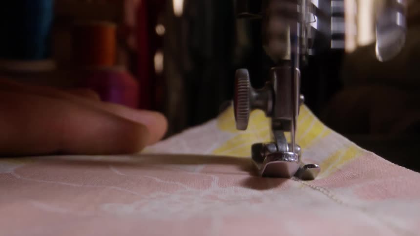 Person sewing cloth with a sewing machine holding it under the needle