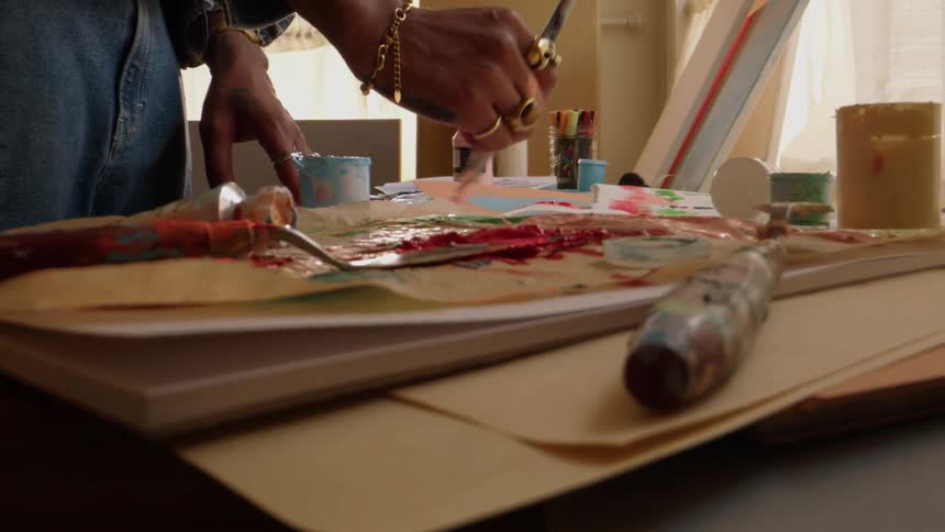 A hand of a person using a brush to paint a cardboard that is above a table