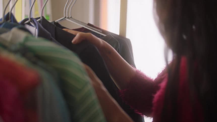 Person chooses clothes from a clothes rack illuminated by daylight
