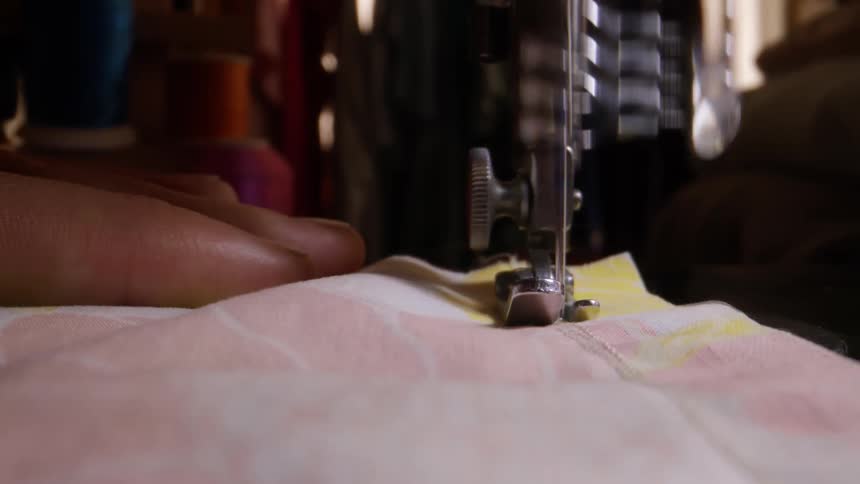 Woman moves fabric under a sewing machine during the daytime