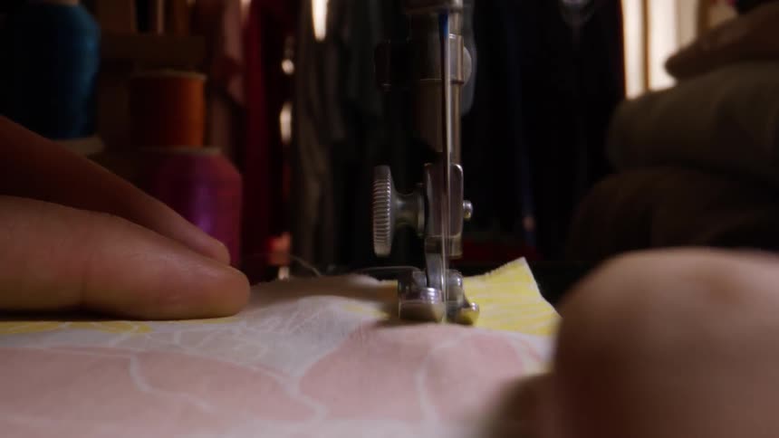 A sewing machine is stitching the surface of a pink fabric with yellow
