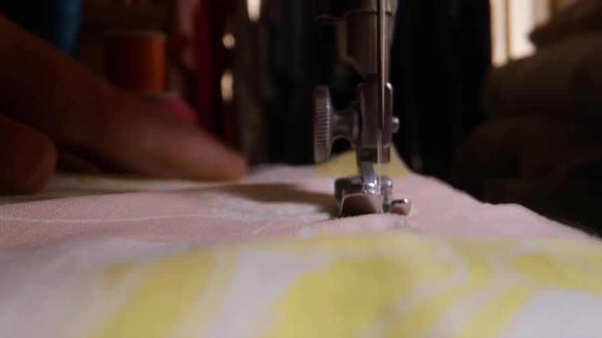 The person holds the fabric as they run a sewing machine over it