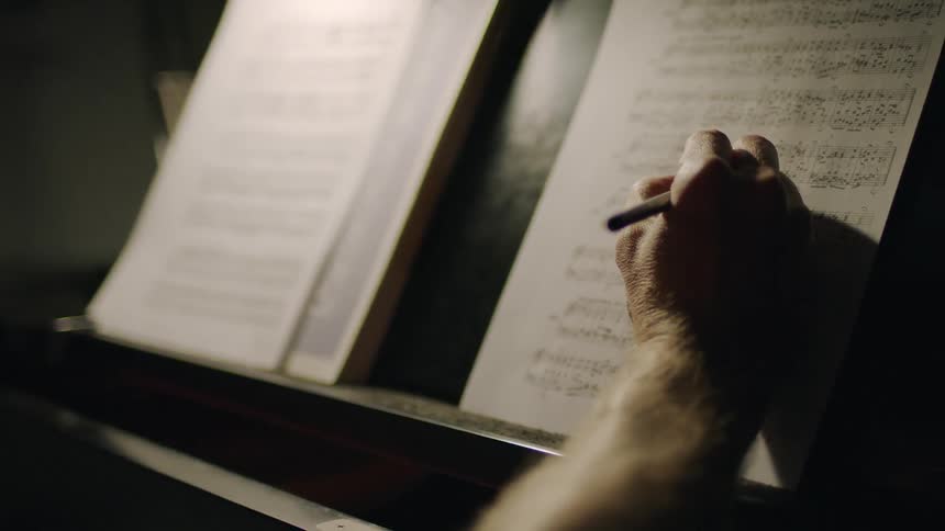 A man is writing on sheet music on a piano