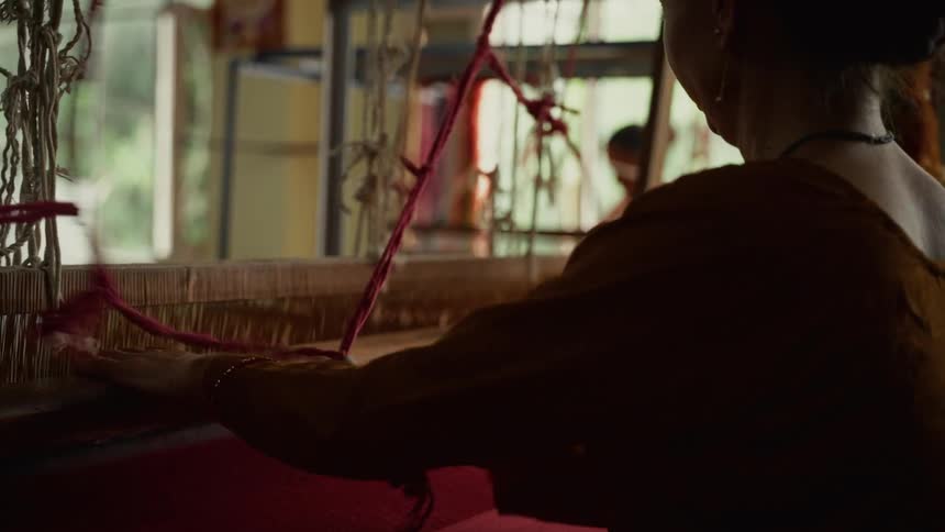 Person weaving manually on loom with red and white threads