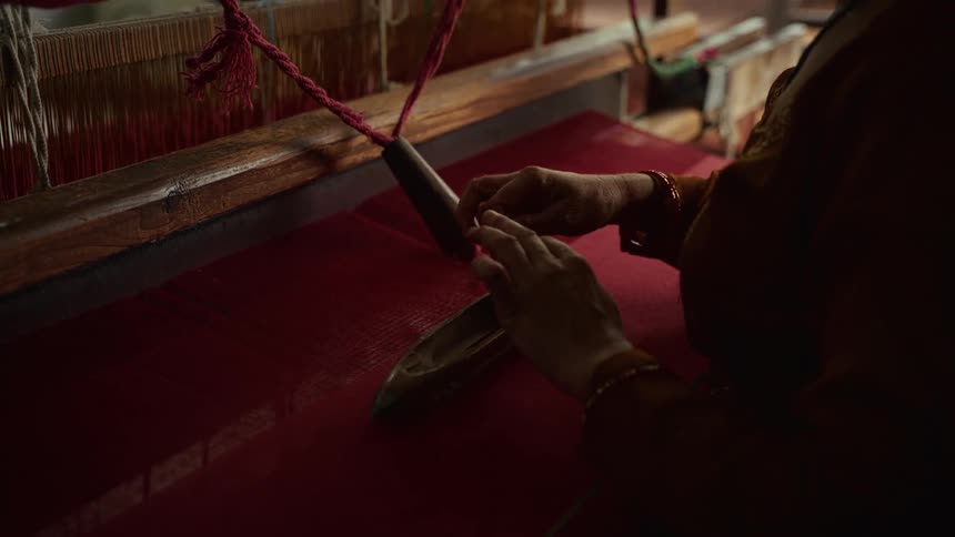 A woman inside a factory sets up thread in a machine preparing it to weave knitwear