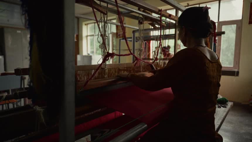 A young woman works inside a knitting factory at midday rolling the machine as she knits fabric