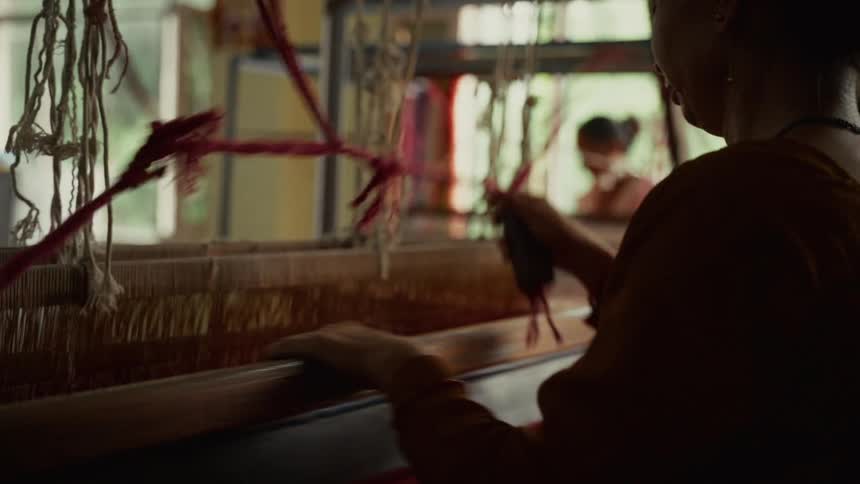 Person weaving red fabric on handloom in naturally lit workshop setting