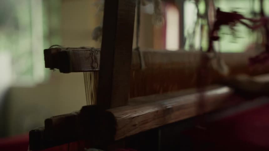 This is a closeup shot of the mechanism of a traditional wooden handloom being operatedthe wooden beams and vertical threads move as the shuttle is passed through indicating the weaving process is underway