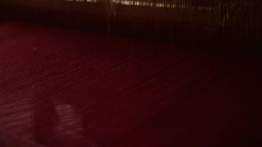 Red threads stretched on traditional loom with visible wooden and metal components