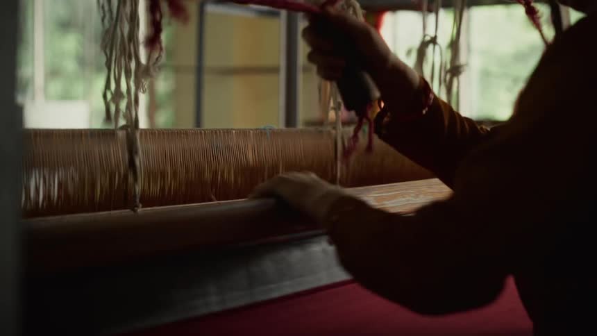 A young woman operates a knitting machine in a factory at midday producing red fabric