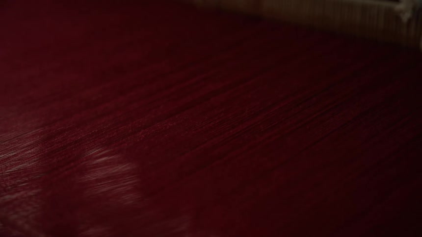A close up of a dark reddishmaroon surface of thread or fabric that exhibits subtle diagonal streaks and a soft sheen
