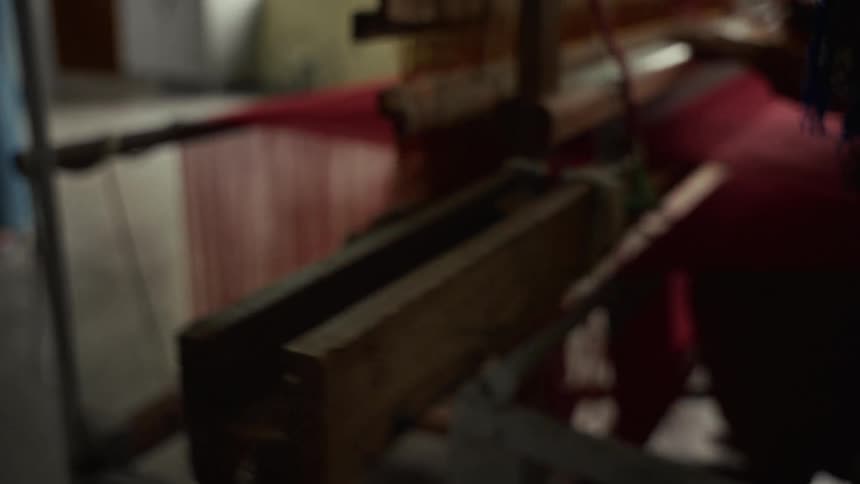 A woman operates a knitting machine in a factory at midday producing red fabric