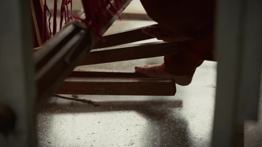 A persons bare feet rhythmically operate the wooden pedals of a traditional loom the steady motion echoing the craft of weaving in a sunlit workshop