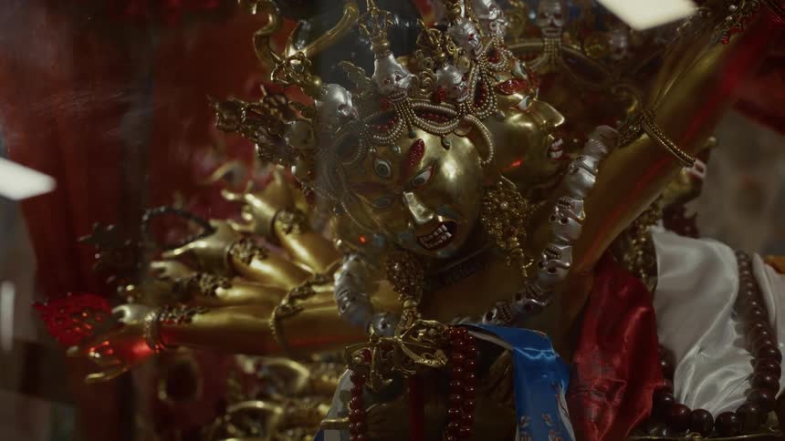 A closeup focuses on an elaborate wrathful deity statue featuring multiple gold faces many arms and intricate skulladorned crowns draped with strings of red beads and colored sashes