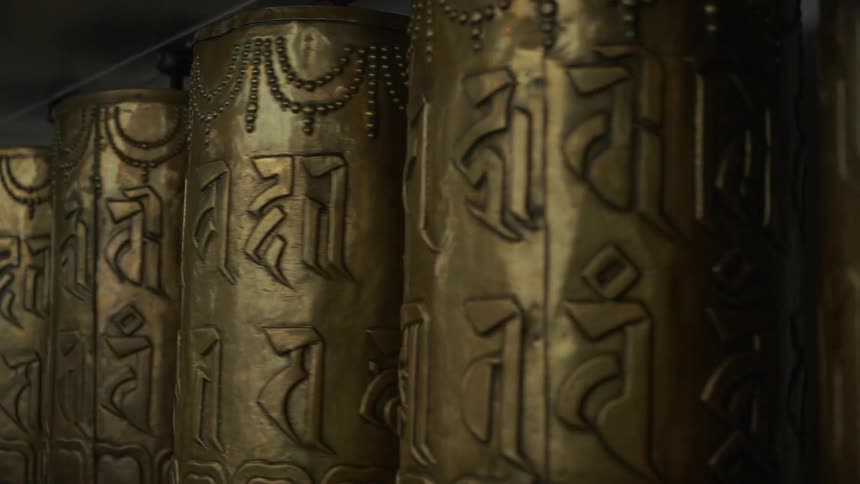 A row of golden tibetan prayer wheels engraved with script spins slowly