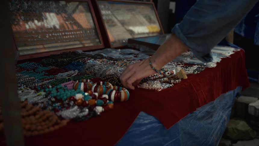 Person picks up a collection of colorful beaded accessories displayed on a table at an outdoor market