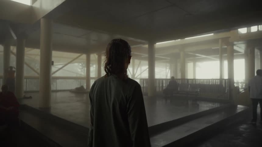 Person walking through large indoor space with columns and seated individuals in traditional attire