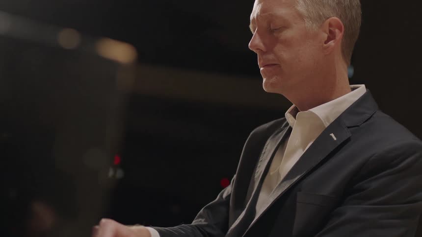 A man in a black suit jacket is playing piano with his eyes closed