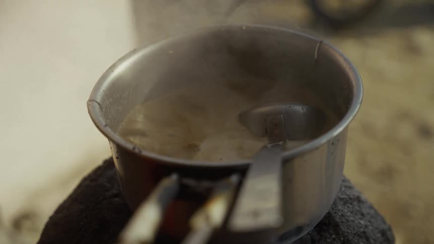 Metal pot with boiling liquid releasing steam in rustic cooking setting