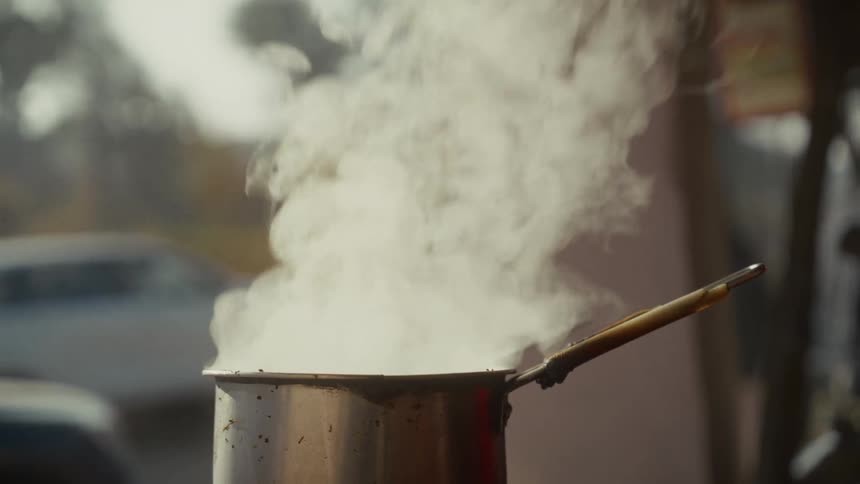 Person cooks in a steaming pot while standing outdoors during the daytime