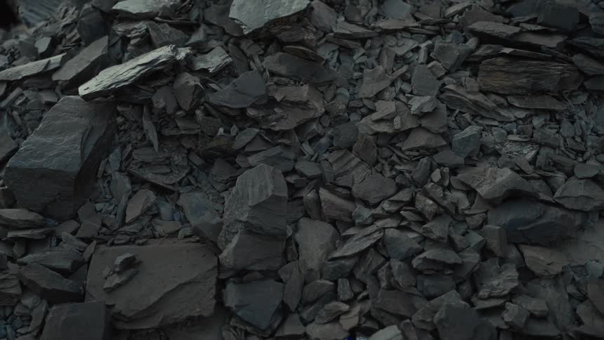 A static detailed closeup shot shows a large heap of dark gray angular and mostly flat fragments of broken rock resembling a pile of quarried slate or shale