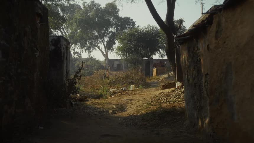 Rural path between old structures with dry vegetation and plastic containers scattered on the ground