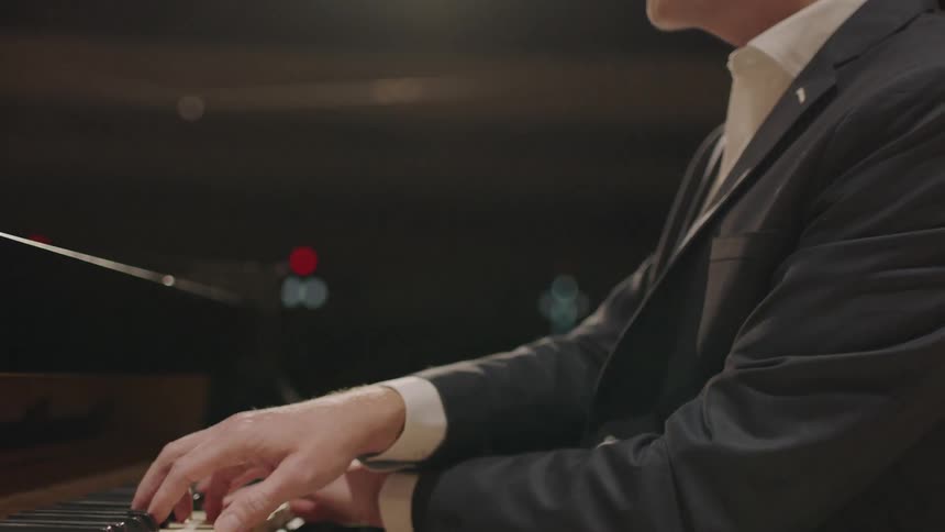 Side view of a man playing a piano at a large venue