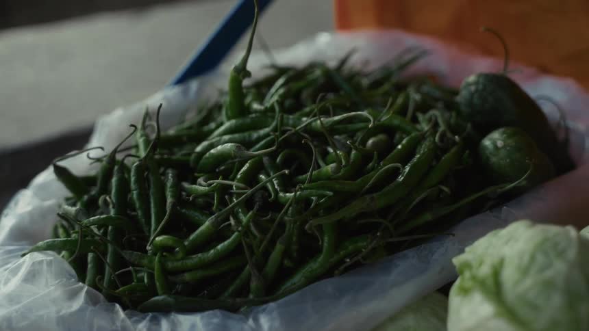 Fresh green chili peppers spread on white sheet beside other vegetables at market stall