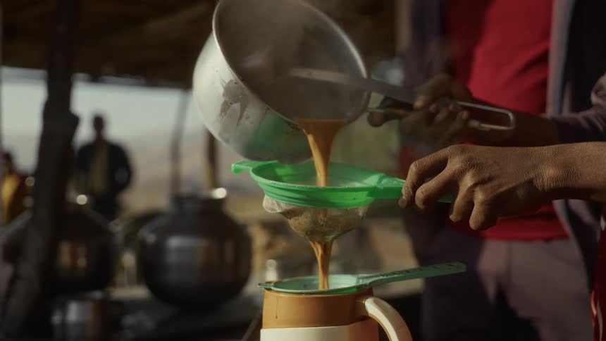 An adult pours hot sauce from a pan into a sieve