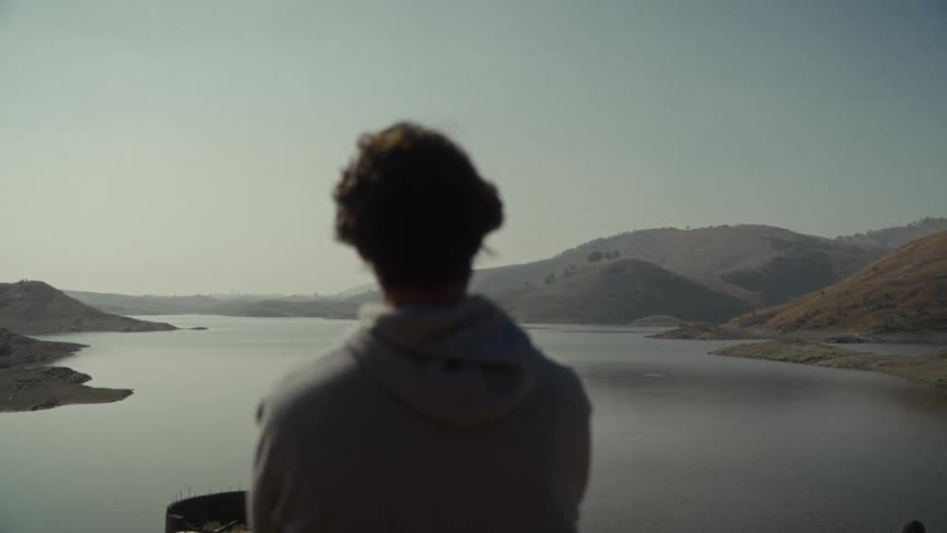 Curlyhaired person overlooking calm lake surrounded by mountains at dusk