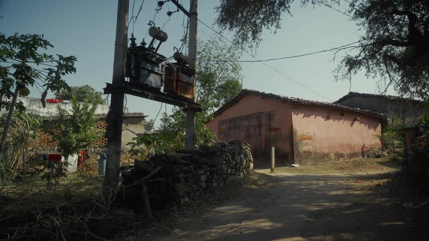 Rural village scene with dirt road electrical transformer and modest houses surrounded by vegetation