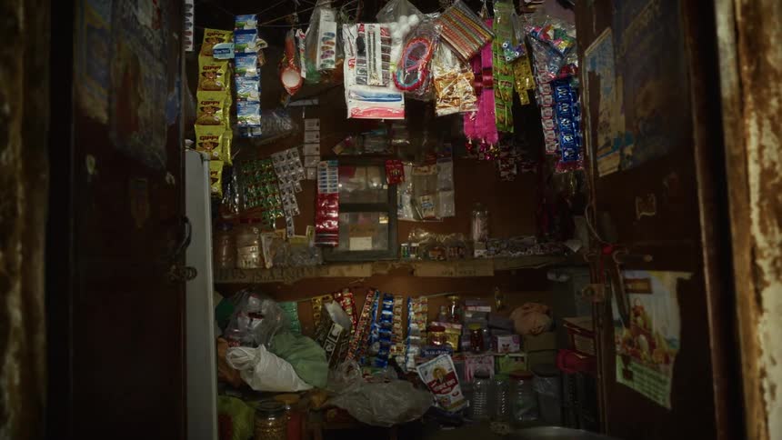 A retail shop with its doors wide open shows building walls covered in rusty paint while the small choice shop inside is filled with goods