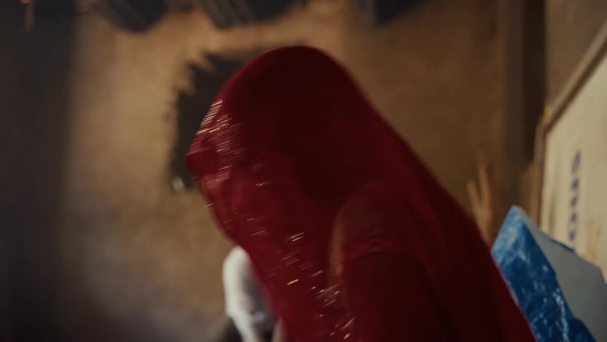This brief video clip features a closeup of a person likely a woman with their head and face covered by a traditional bright red veil or ghunghat in the dimly lit background a person wearing a white shirt is blurred and out of focus