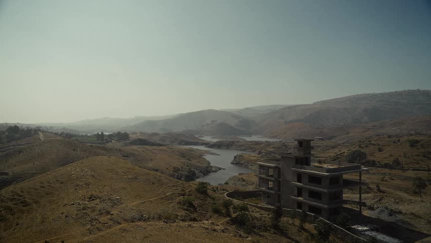 Lone multi story building stands near a riverbank on a foggy hilly day