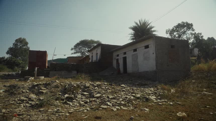 Simple buildings in a rural area with sparse vegetation and a person near a house entrance