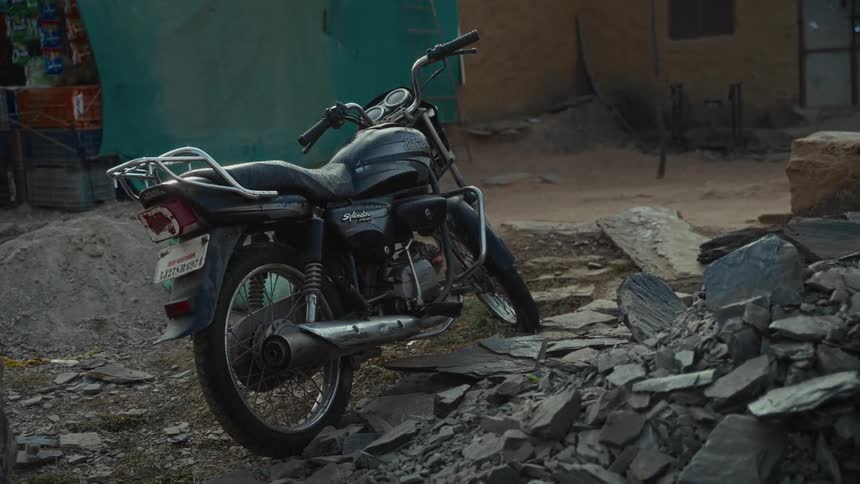 A black motorcycle is parked on a dirt path amidst piles of jagged gray rocks