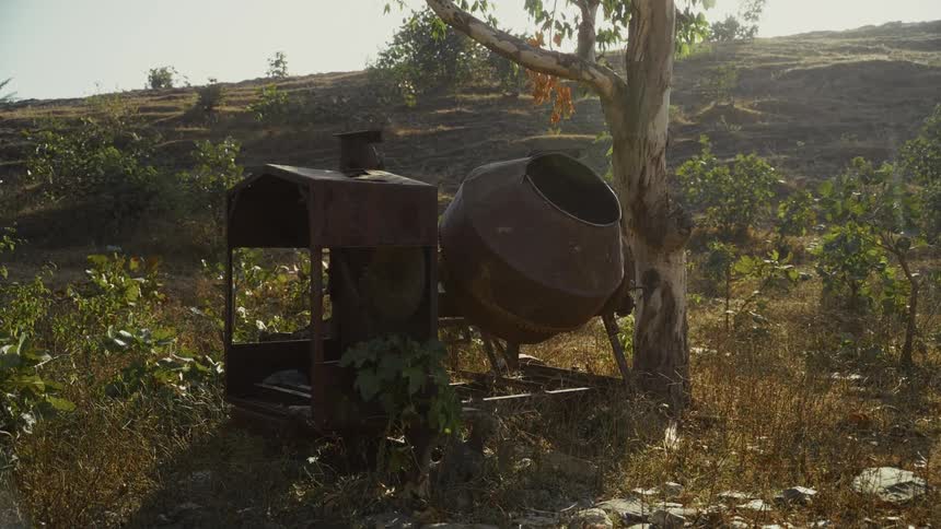 Rusty concrete mixer placed on dry ground with sparse vegetation and hills in the background