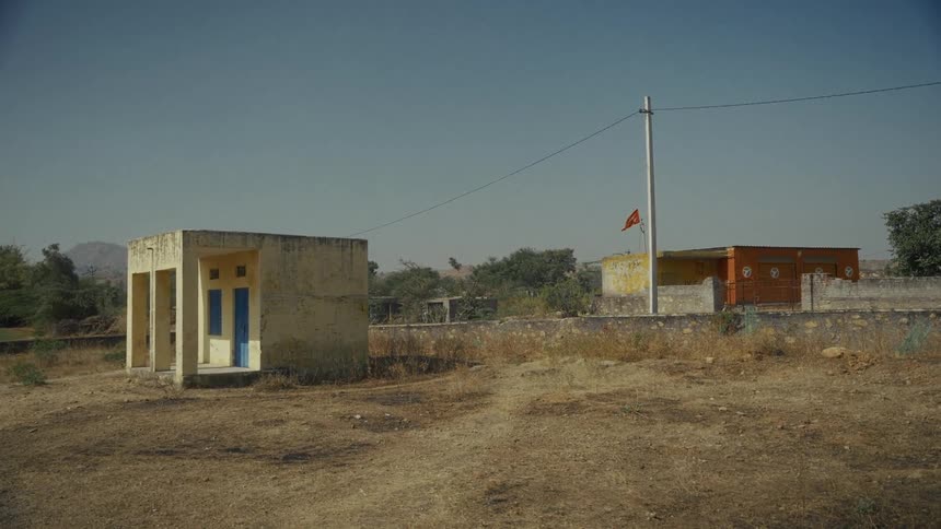 Rural scene with two modest buildings in dry field one with blue doors and another with red flag